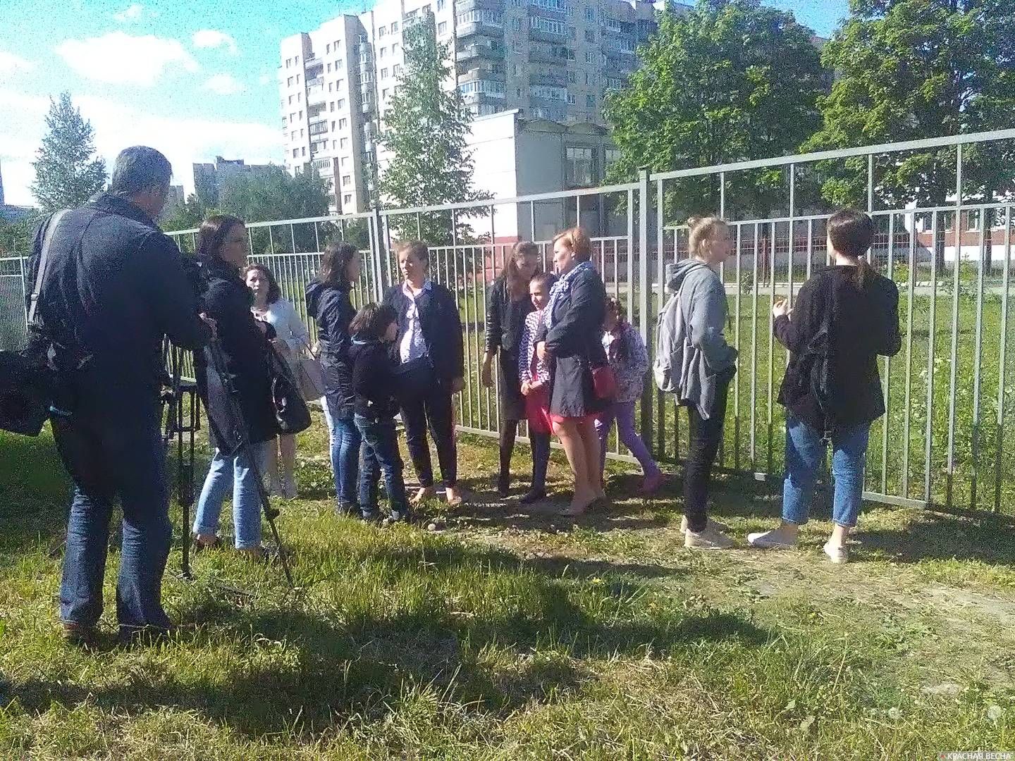 Родители и ученики собираются на поляне за территорией школы для общения со СМИ