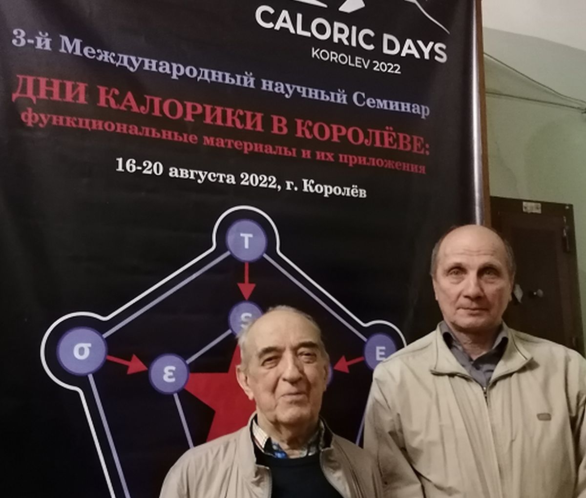 Профессор  Владимир Шавров  (слева) и  доктор физико-математических наук Виктор Коледов (справа) на фоне плаката по международной конференции по калорике 