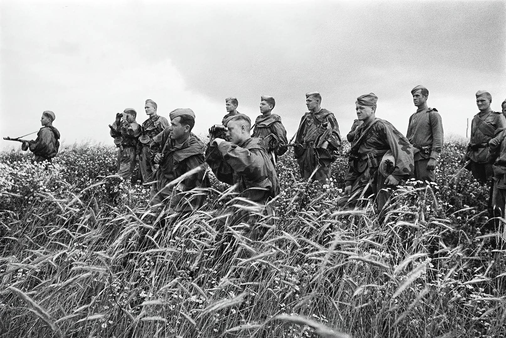 Бойцы РККА (предположительно, из разведгруппы), стоя в поле, наблюдают за ходом боя. 1944