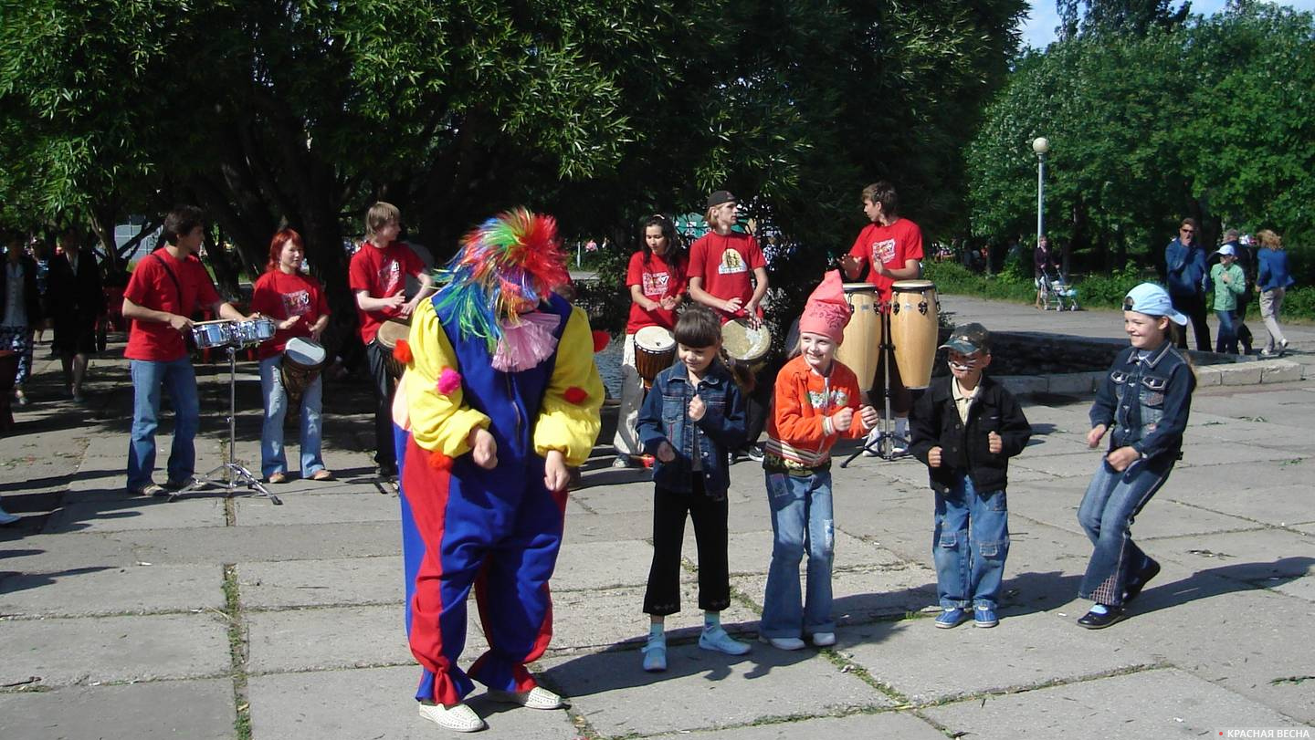 Клоун и дети танцуют под звуки этнических барабанов