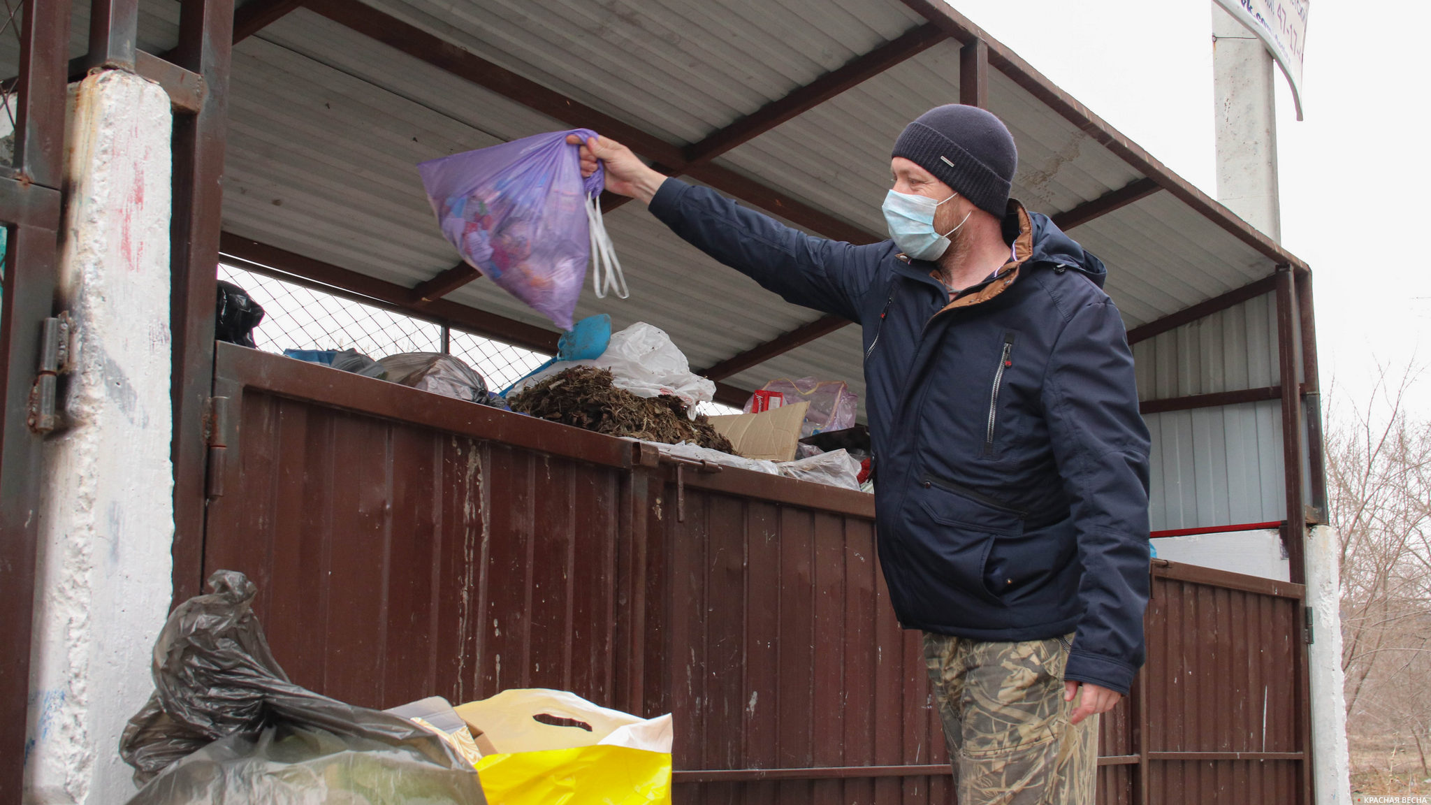 Человек в защитной маске выкидывает мусор