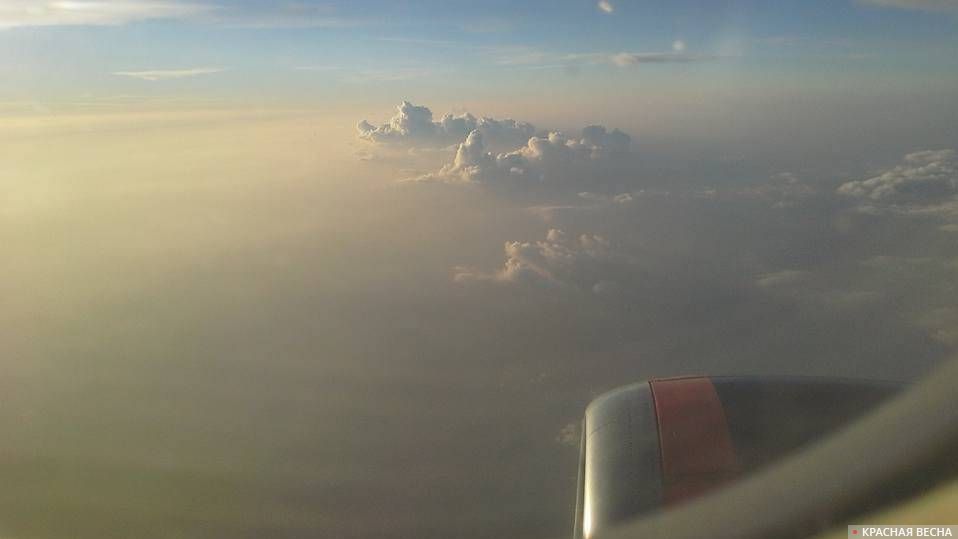 Вид на облака и землю через иллюминатор самолёта