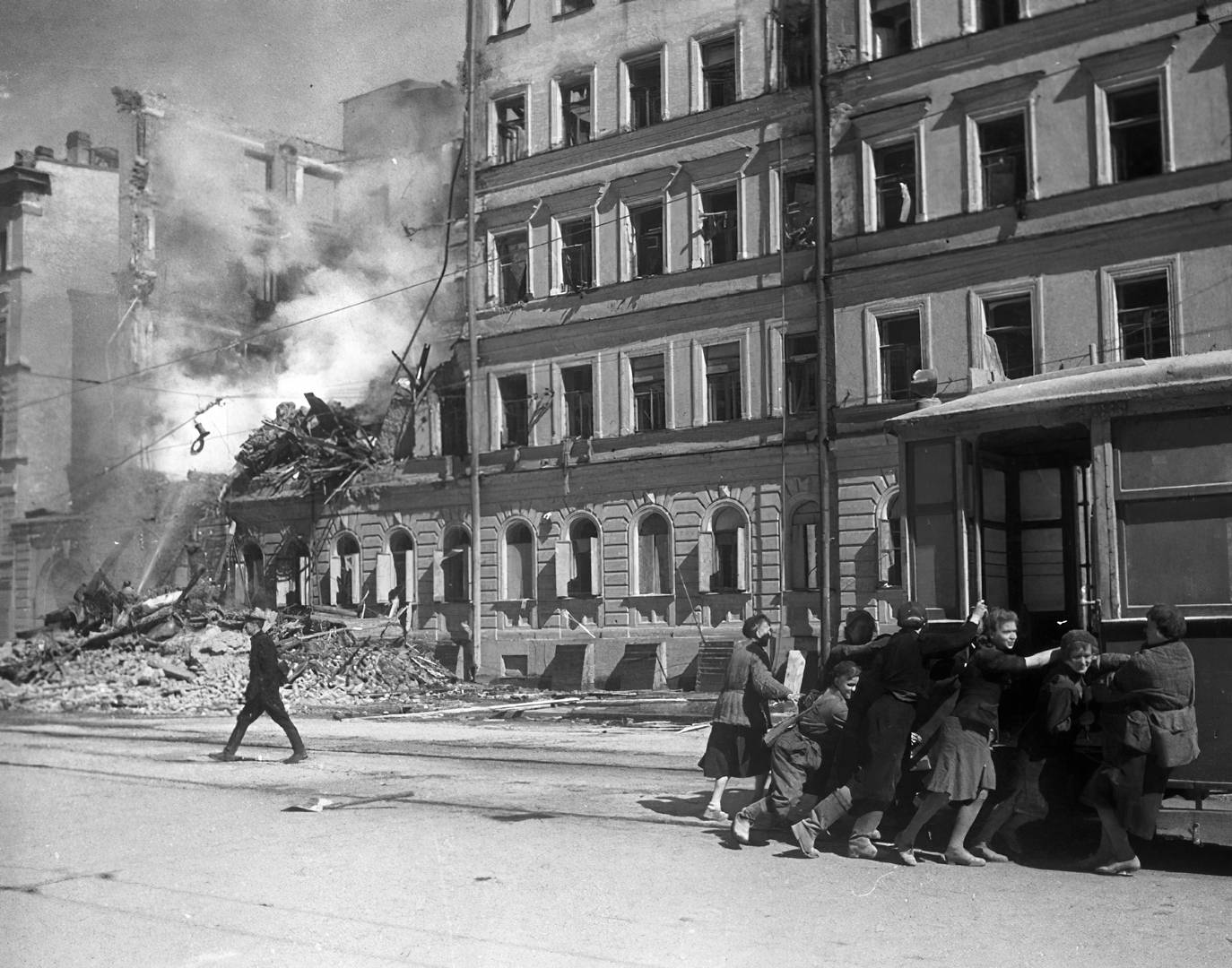 Жители блокадного Ленинграда передвигают трамвайный вагон подальше от фасада разрушенного бомбардировкой дома. 1942 г.