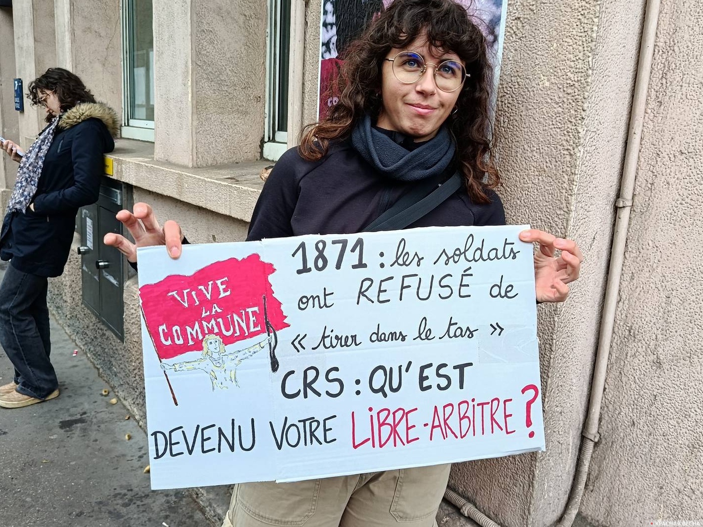 В руках у девушки — плакат: «Да здравствует Коммуна! 1871: солдаты отказались стрелять в толпу. А где теперь свобода действий у CRS?»