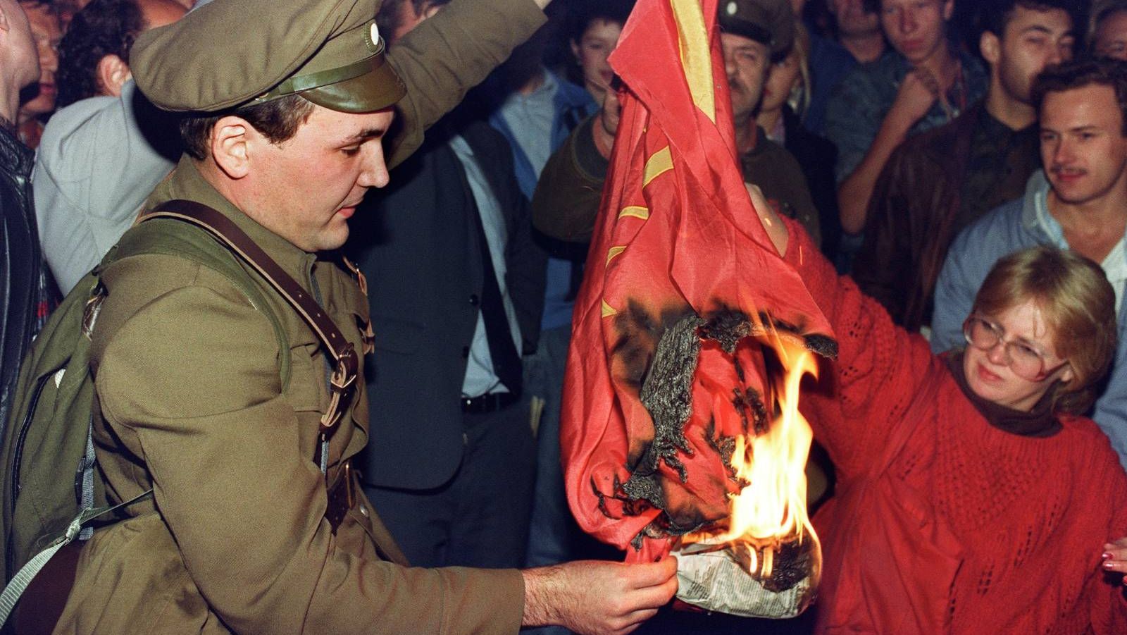 Человек, одетый в дореволюционную форму, сжигает советский флаг во время митинга в Москве 1991г