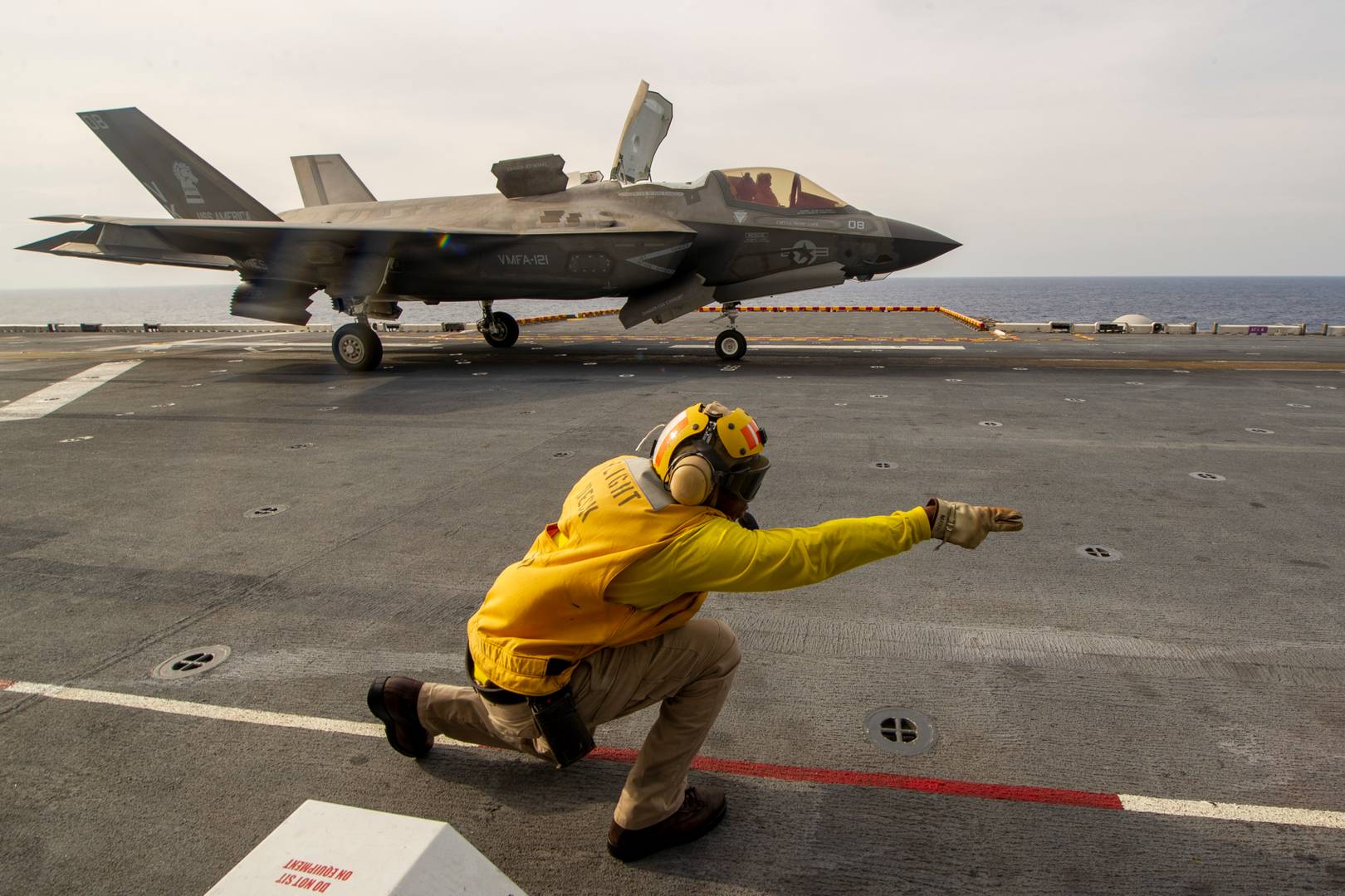 Служащий летной палубы дает команду на взлет пилоту истребителя F- 35B Lightning II с палубы десантного корабля USS America (LHA 6)