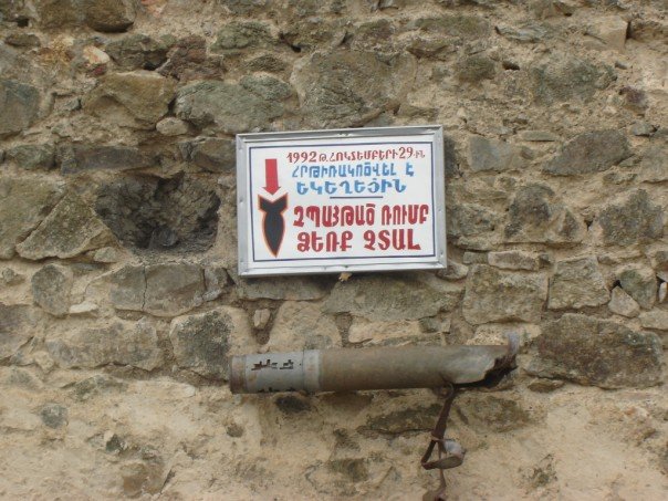 Внешняя стена Гандзасара. 2005 год. Надпись на армянском на табличке — «Церковь была обстреляна 29 октября 1992 года. Невзорвавшийся снаряд. Руками не трогать»