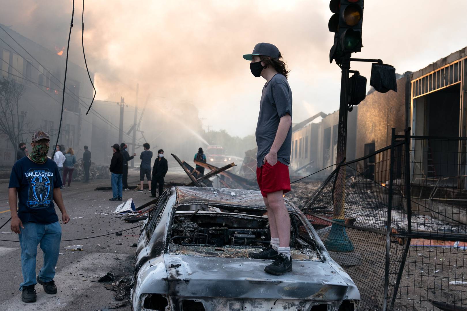Человек в маске стоит на сожженной машине. Протесты в США
