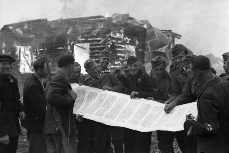 Солдаты вермахта и литовские полицейские со свитком торы на фоне горящей синагоги. 1941